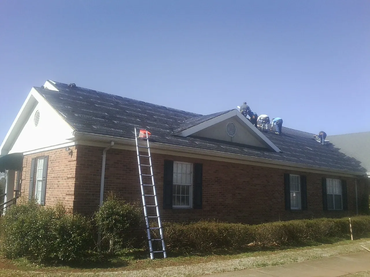 Crew tearing shingles off a brick ranch roof with a ladder set — Metal Roof Repair work by our crew in Wells