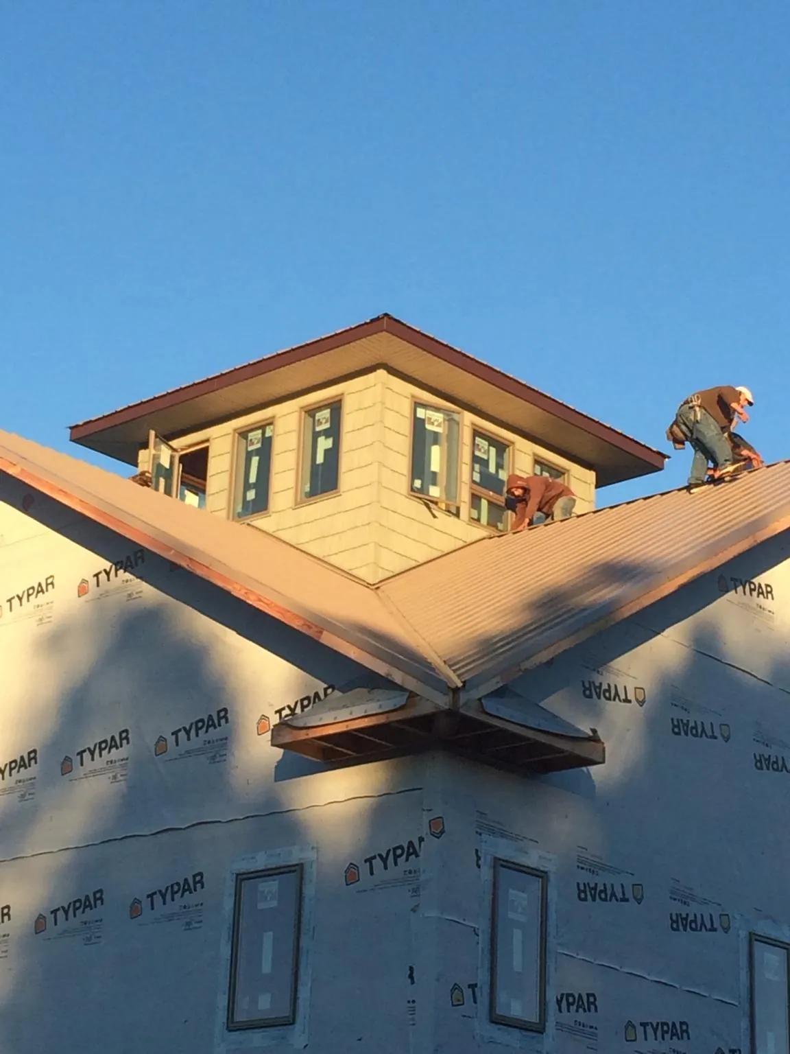 Roofers working around a rooftop cupola on a new metal roof at sunset — Roof Waterproofing in Wells by Roofing Brothers
